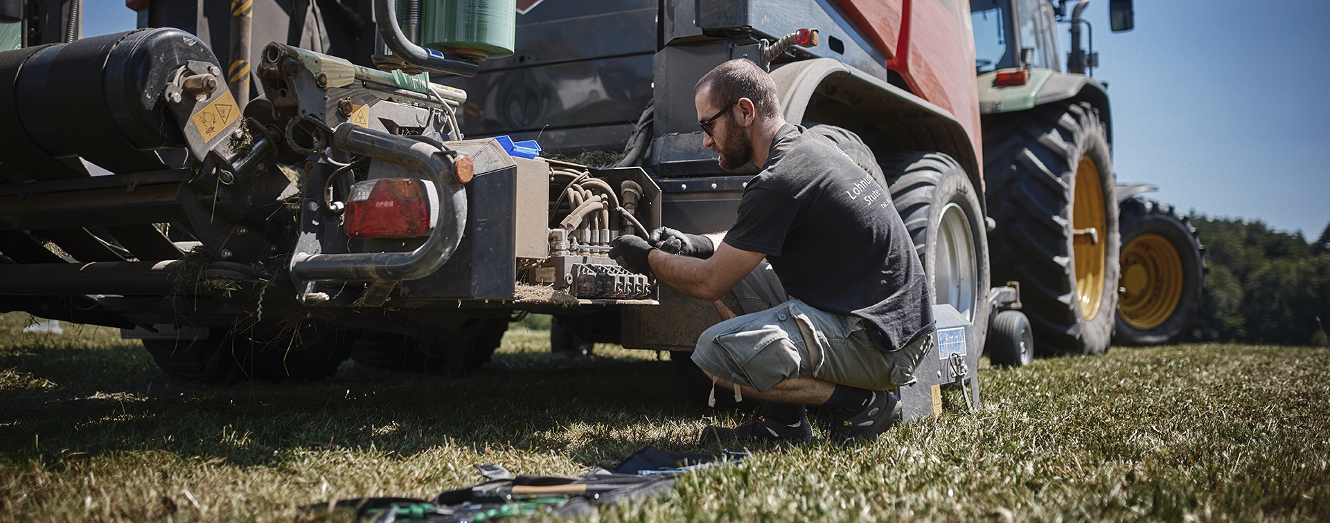 En mand i marken reparerer en ballepresser med en skruenøgle