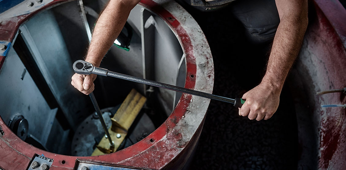 Employee using ratchet with extra long lever on a machine
