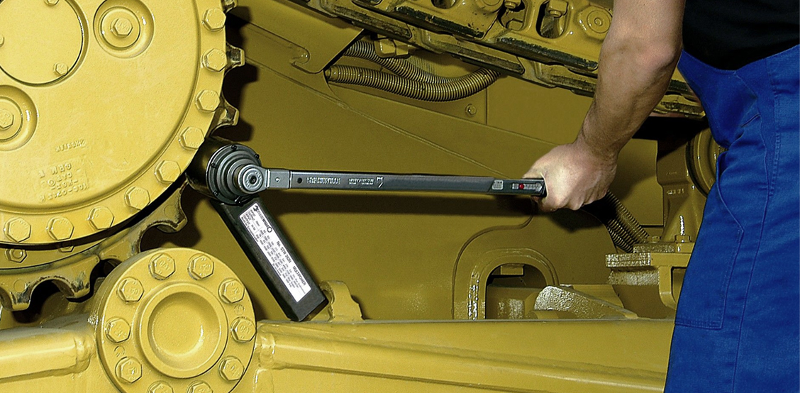 A STAHLWILLE torque multiplier in combination with a torque wrench is used to precisely tighten a large bolted connection on a construction site vehicle.